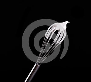 Metal whisk with whipped egg whites, isolated on black background. Clipping path.