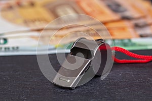 Metal whistle with Euro banknotes on slate