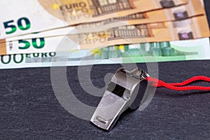 Metal whistle with Euro banknotes on slate