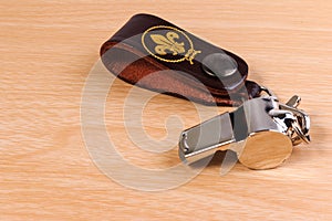 Metal whistle with leather key chain on wooden background.