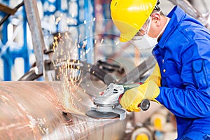 Metal worker in factory grinding metal of pipeline