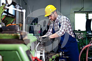 Metal worker turner operating lathe machine at industrial manufacturing factory.