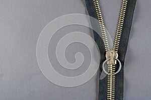 Metal zipper on gray background. Clasp with yellow prongs and bl