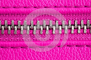 Metal zipper on intense pink purple leather jacket or purse detail close up macro. The zipper is tightly closed.