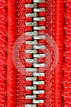 Metal zipper on intense red leather jacket or purse detail close up macro. The zipper is tightly closed.