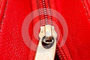 Metal zipper on intense red leather jacket or purse detail close up macro. The zipper is partly open and binding together layers