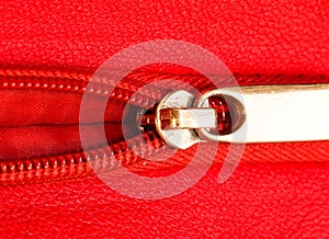 Metal zipper on intense red leather jacket or purse detail close up macro. The zipper is partly open and binding together