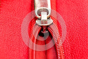 Metal zipper on intense red leather jacket or purse detail close up macro. The zipper is partly open and binding together