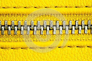 Metal zipper on intense yellow leather jacket or purse detail close up macro. The zipper is tightly closed