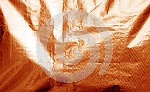 Metalized plastic wrap texture with crumples in orange color