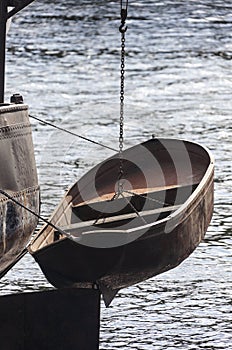 Metallic boat hangs over water on steel chain overboard