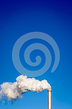 A metallic chimney spitting out white smoke against blue sky