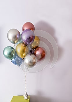 Metallic coloured helium balloons tied with a bow and held by a weight on a green table