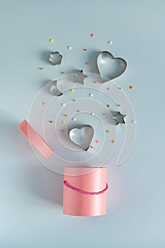 Metallic cookie cutters in heart shape flying out the pink gift box on blue background. Bonus and sale concept. Copy space