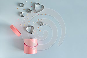 Metallic cookie cutters in heart shape flying out the pink gift box on blue background. Bonus and sale concept. Copy space