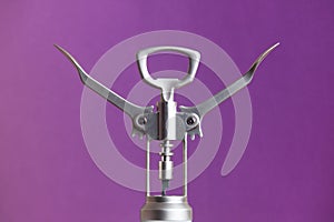 Metallic corkscrew with two levers like humanoid robot raises it`s hands up on a purple background