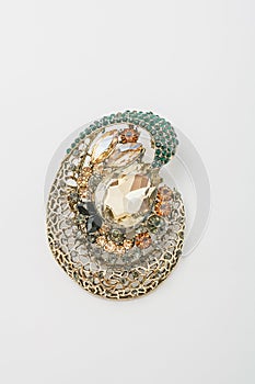 Metallic golden brooch with black, orange, green gemstones imitation, pin on white background, bijouterie, jewelry close up