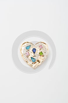 Metallic golden brooch in shape of heart with bright gemstones imitation, pin on white background, bijouterie, jewelry close up
