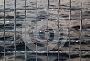 Metallic net with drops against sea background.