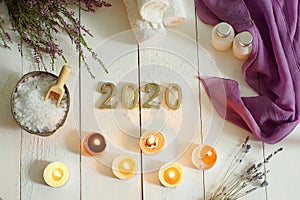 Metallic numbers 2020 on a background of white boards next to towels and sea salt for spa treatments, scented candles and a sprig
