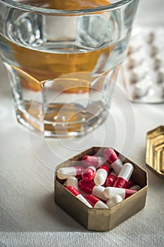 Metallic pillbox with white and red capsules along with water glass