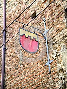 Metallic plaque of a Medieval Embattled Shield on a brick facade. Asti, Piedmont, Italy