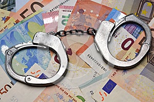 Metallic police handcuffs on euro banknotes suggesting corruption or criminal delinquency