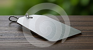 A metallic rectangular tag with rounded edges lies on a wooden surface. The tag