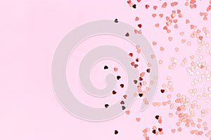 Metallic red confetti in a heart shape scattered on a pink background.