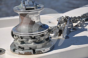 Metallic rusty anchor windlass on a white boat at the sea. Anchor is pulled up with the winch and chain. Metal looks shiny in the