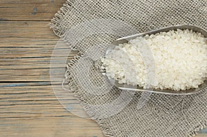 Metallic scoop with rice on wooden background