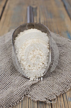 Metallic scoop with rice on wooden background