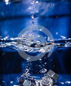 Metallic shiny parts fall into the liquid, air bubbles appear in the water.