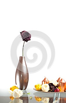 Metallic vase with one rose flower on the table over white. Modern decoration with vase, flowers and candles on a plate