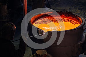 A metallurgical worker at a large vat with molten metal