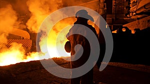 Metallurgist worker in protective uniform at the steel plant controlling hot molten metal pouring process. Man working