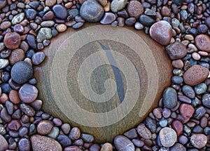 A metamorphic siltstone border with striations on a shingle beach in Scotland surrounded by smooth pebbles.