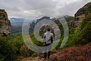 Meteora - Man with scenic view of Holy Monastery of Rousanos and Holy Monastery St Nicholas Anapafsas appearing from fog.