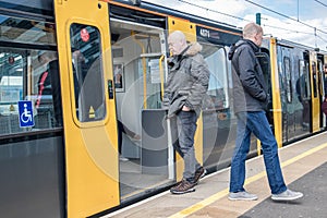 Metro light rail train on a platform in station with people boarding and exiting open doors