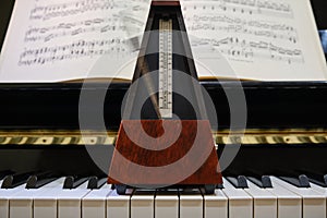 Metronome in motion on a piano with a music sheet in background