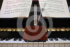 Metronome in motion on a piano with a music sheet in background