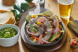 Mexican beef fajitas in iron skillet with guacamole and beer