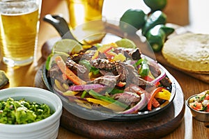 Mexican beef fajitas in iron skillet with guacamole and beer