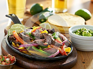 Mexican beef fajitas in iron skillet with guacamole and beer