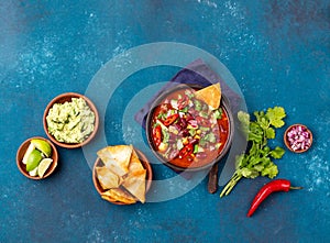 Mexican black bean soup with tomato, avocado and totopos. Blue background, top view