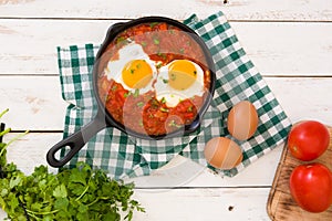 Mexican breakfast: Huevos rancheros in iron frying pan on white wooden table top view