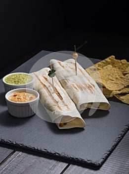 Mexican burritos with cheese sauces and guacamole with black background photo
