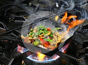 Mexican chicken fajitas on sizzling plate with fire and smoke