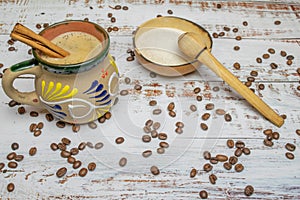 Mexican coffee with cinnamon in cup with Mexican decoration on white wooden table with organic coffee grain and natural bowl with