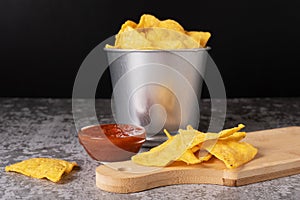 Mexican corn chips in a metal bucket and on a wooden board. Selective focus on chips on the table